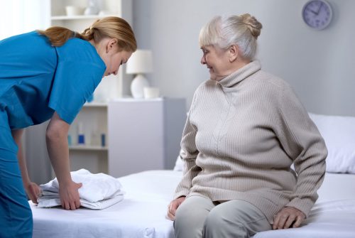 Nurse preparing clean bed-linen to elderly female patient in medical center