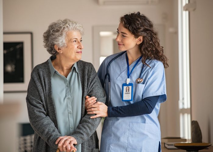 Young caregiver helping senior woman walking. Nurse assisting her old woman patient at nursing home. Senior woman with walking stick being helped by nurse at home.