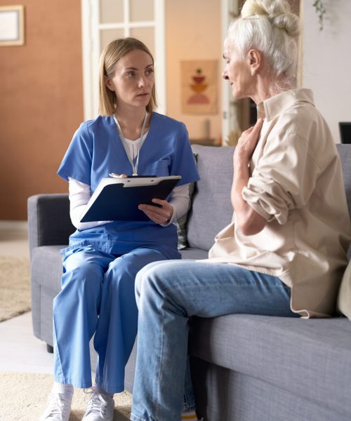 Vertical image of senior woman complaining on her health to doctor while they sitting on sofa in the living room